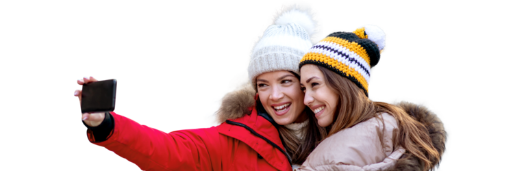 Zwei Frauen stehen lächelnd nebeneinander und schauen auf ihr Handy