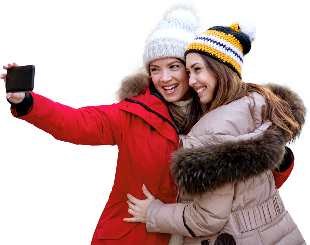 Zwei Frauen stehen lächelnd nebeneinander und schauen auf ihr Handy