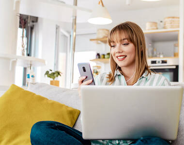 Das Bild zeigt eine Frau mit Laptop und Smartphone